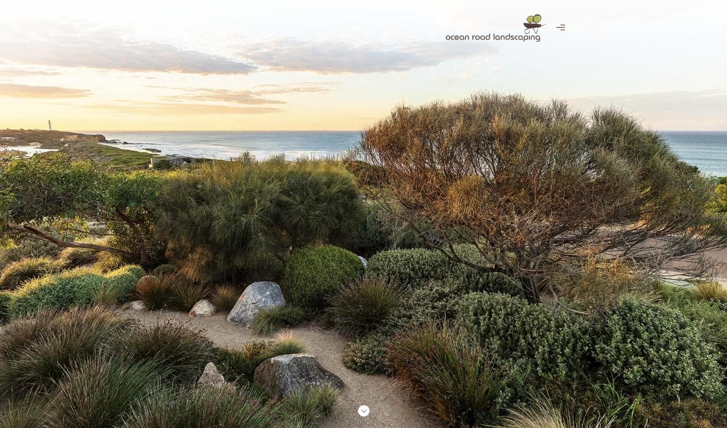 Ocean Road Landscaping homepage — a native coastal garden of native grasses and banksia overlooking the ocean and a lighthouse at sunset